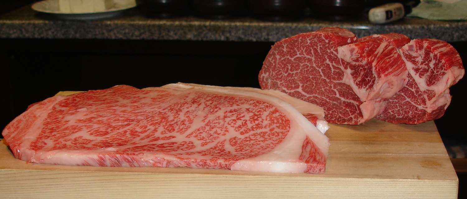 Two raw Kobe cuts on a wooden board, the marbling the grade is read from