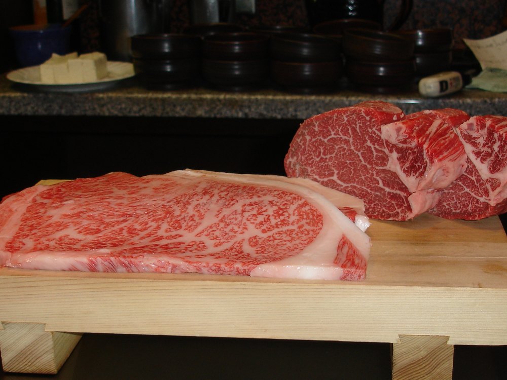 Two raw Kobe cuts on a wooden board, the marbling the grade is read from