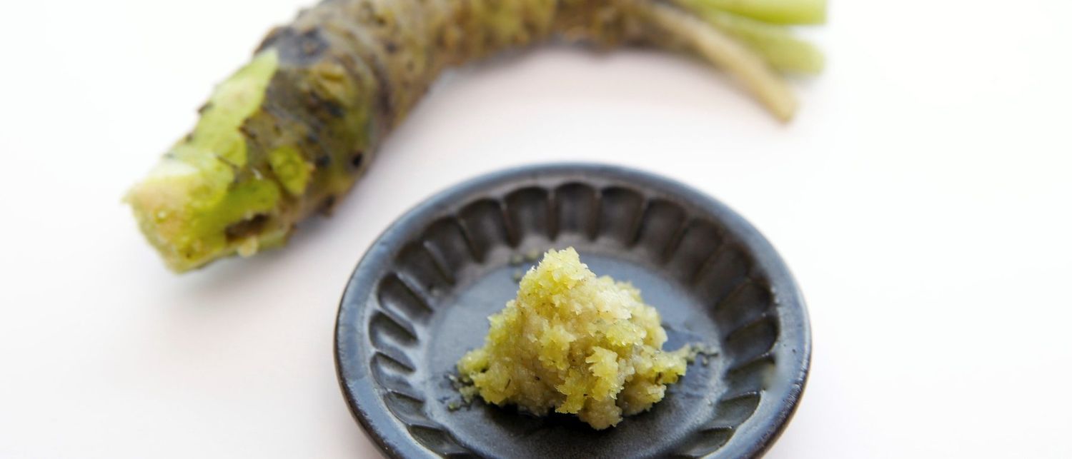 A fresh wasabi rhizome beside grated wasabi on a dark dish